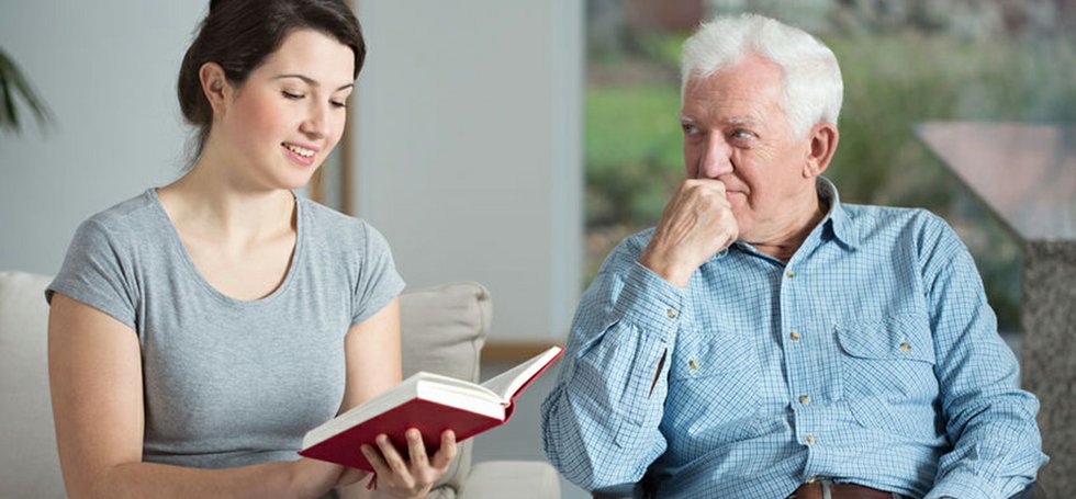 a young female live in caregiver reading to an elderly man in one of their Harris county facilities